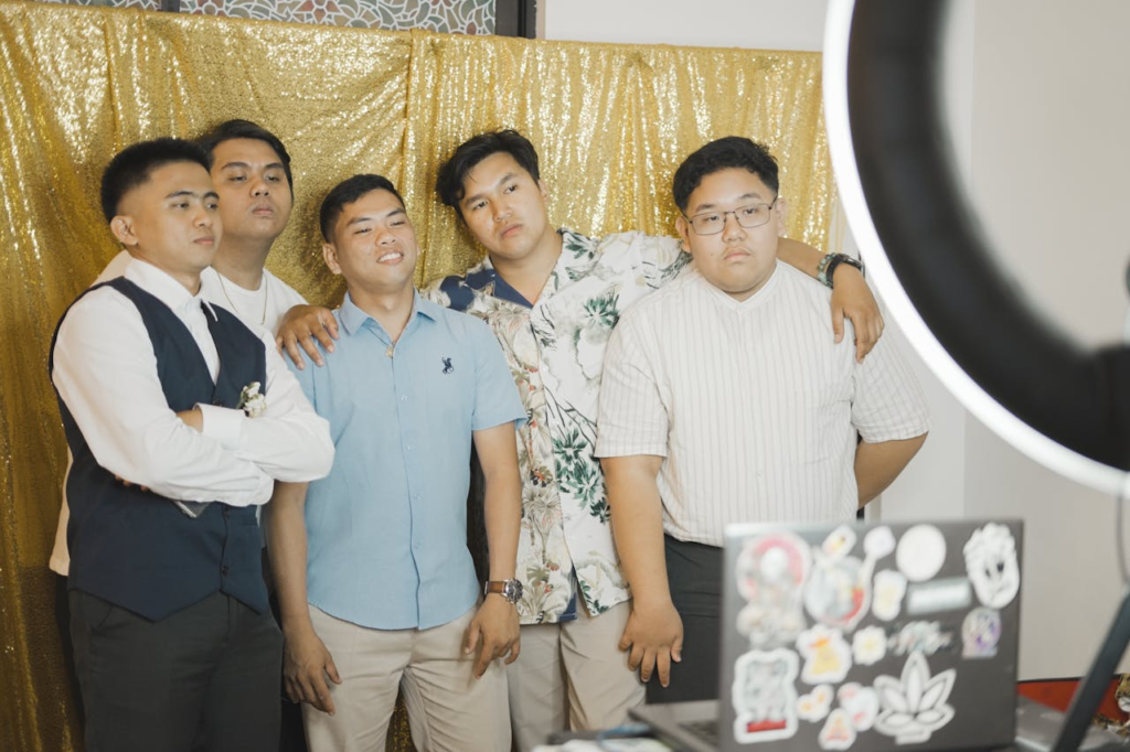 Five young men pose together against a gold backdrop, capturing a fun and friendly moment.