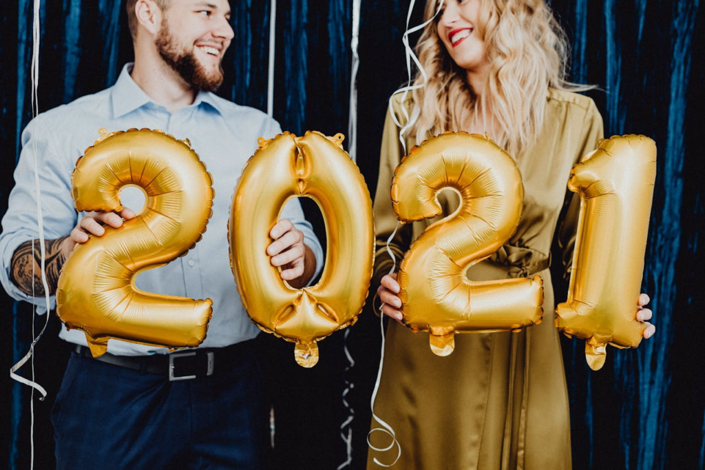 Smiling couple holding gold balloons forming 2021 for a festive New Year's celebration.