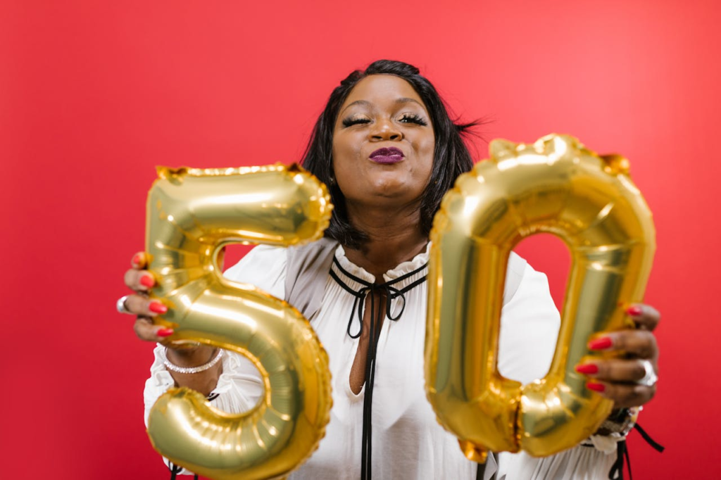 Joyful woman holding golden 50 balloons against a vibrant red background.